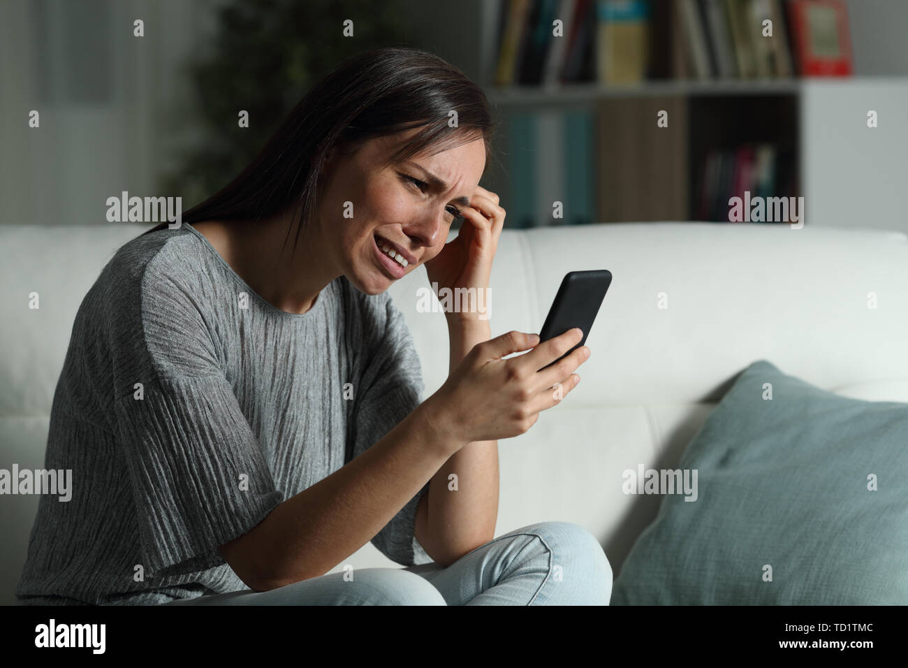 Femme triste contrôle smart phone dans la nuit, assis sur un canapé dans la salle de séjour à la maison Banque D'Images