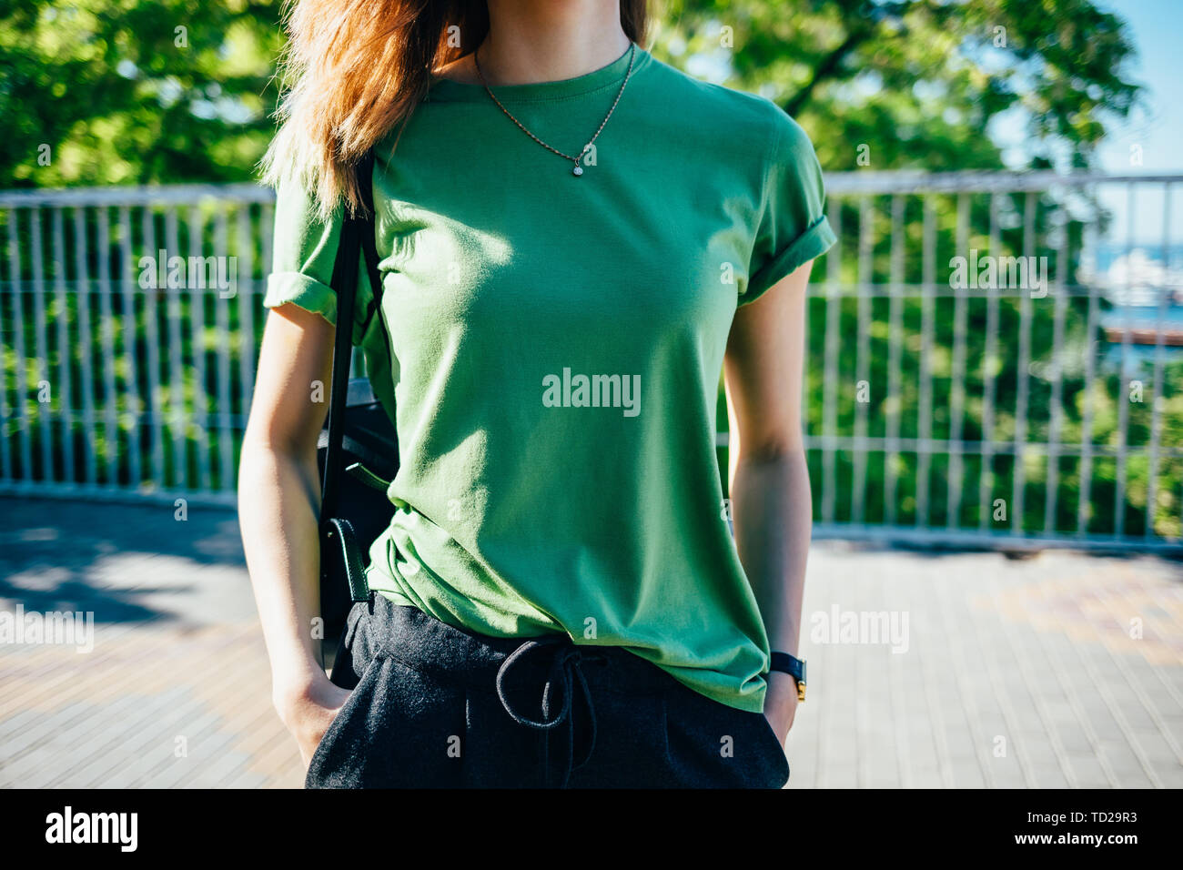 Jeune femme élégante debout à sunny green street. Les femmes vêtus de t-shirt maintenant ses mains dans les poches. Close-up détails de l'été femmes clot Banque D'Images