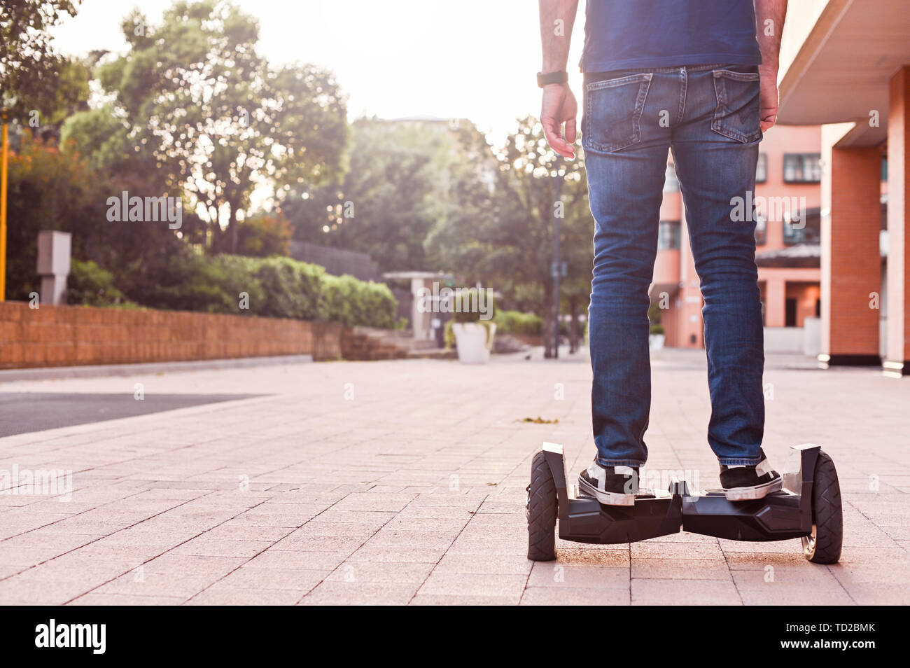 Un homme en jeans et baskets sur un hoverboard ride dans la ville. Happy boy riding autour au coucher du soleil. L'électronique moderne pour la détente et le divertissement Banque D'Images