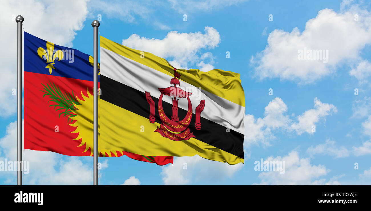 La Guadeloupe et le Brunei drapeaux dans le vent contre ciel bleu nuageux blanc ensemble. Concept de diplomatie, de relations internationales. Banque D'Images
