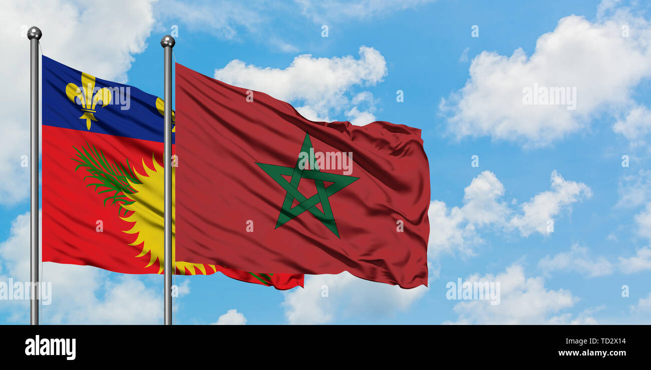 Guadeloupe et de brandir le drapeau du Maroc dans le vent contre ciel bleu nuageux blanc ensemble. Concept de diplomatie, de relations internationales. Banque D'Images