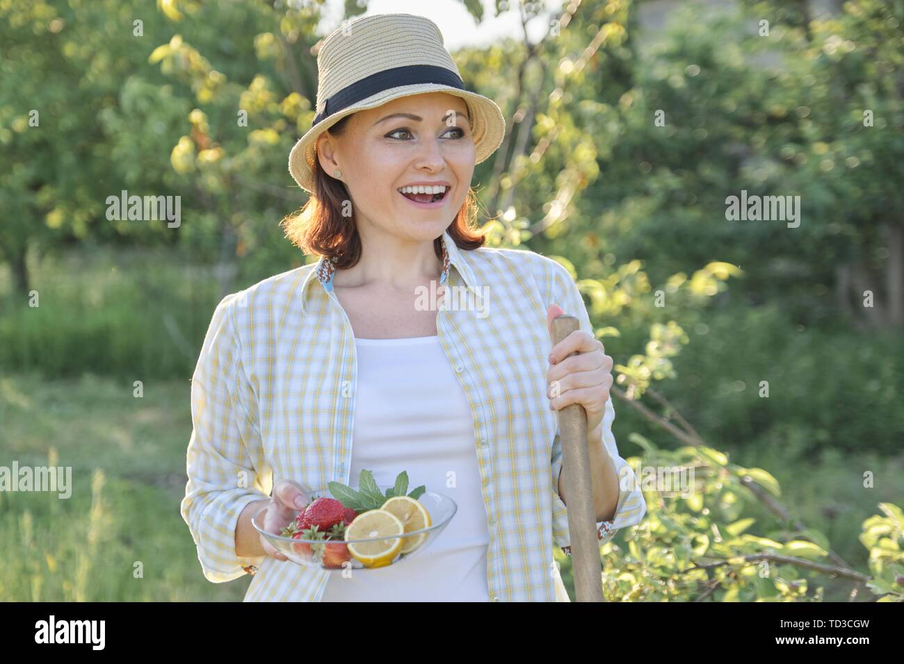 Piscine libre de 40 ans, Femme au chapeau de paille dans le jardin avec la plaque de fraises menthe citron, vacances d'été et travailler dans la nature Banque D'Images