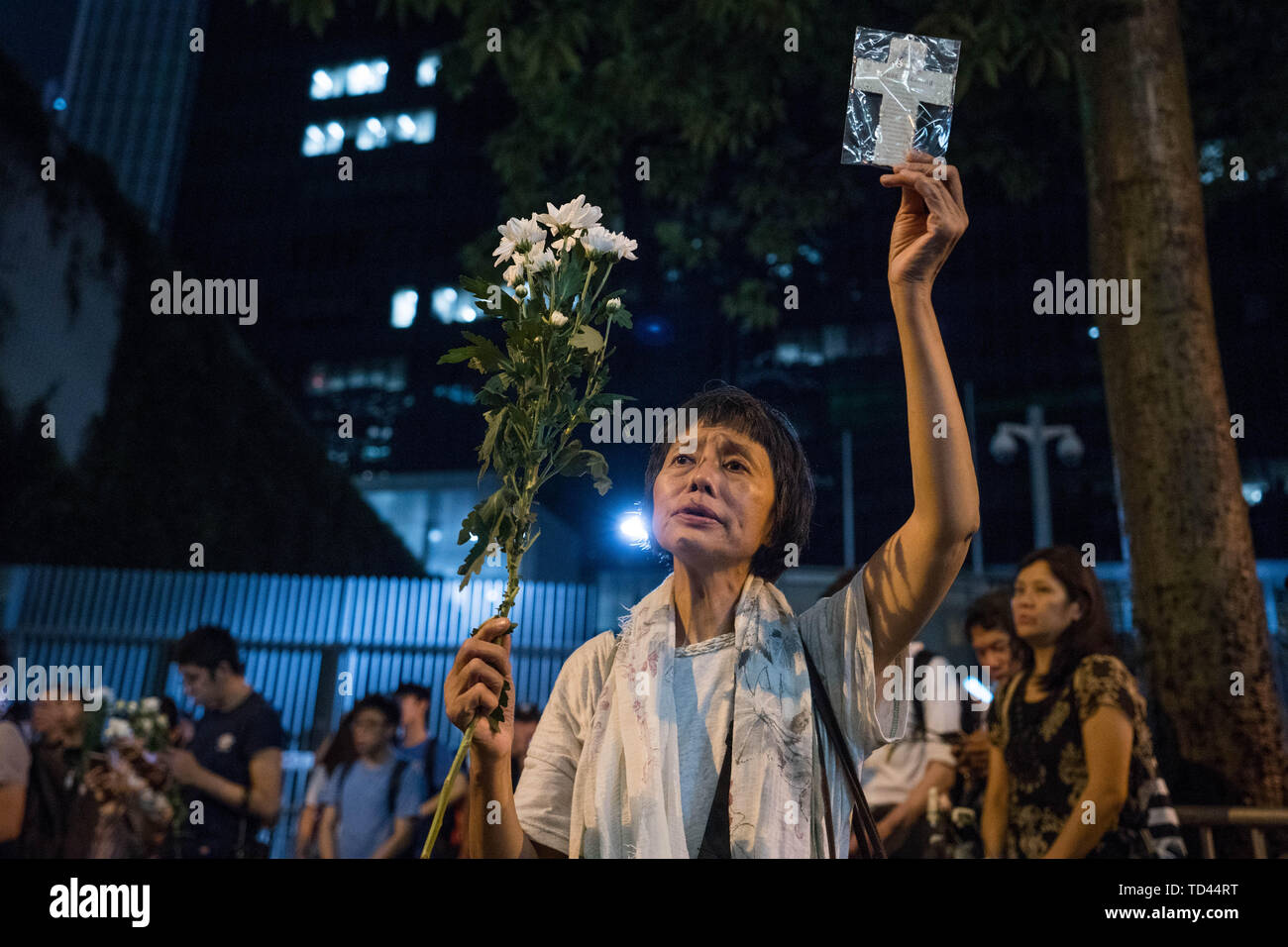 Une femme est titulaire d'une fleur et la croix comme à l'extérieur, elle prie le Conseil législatif complexe dans Hong Kong deux jours après que la ville a vu sa plus grande rue protester dans au moins 15 ans alors que des centaines de milliers de personnes ont défilé contre le plan du gouvernement de présenter le projet de loi pour permettre aux extraditions vers la Chine continentale. Le gouvernement de Hong Kong a refusé d'abandonner un projet de loi controversé pour permettre aux extraditions vers le continent chinois, chef de la carrie Lam a dit que le législateur ne soit discuter du projet de loi le 12 juin comme prévu, rejetant les appels à retarder ou annuler la loi. Banque D'Images