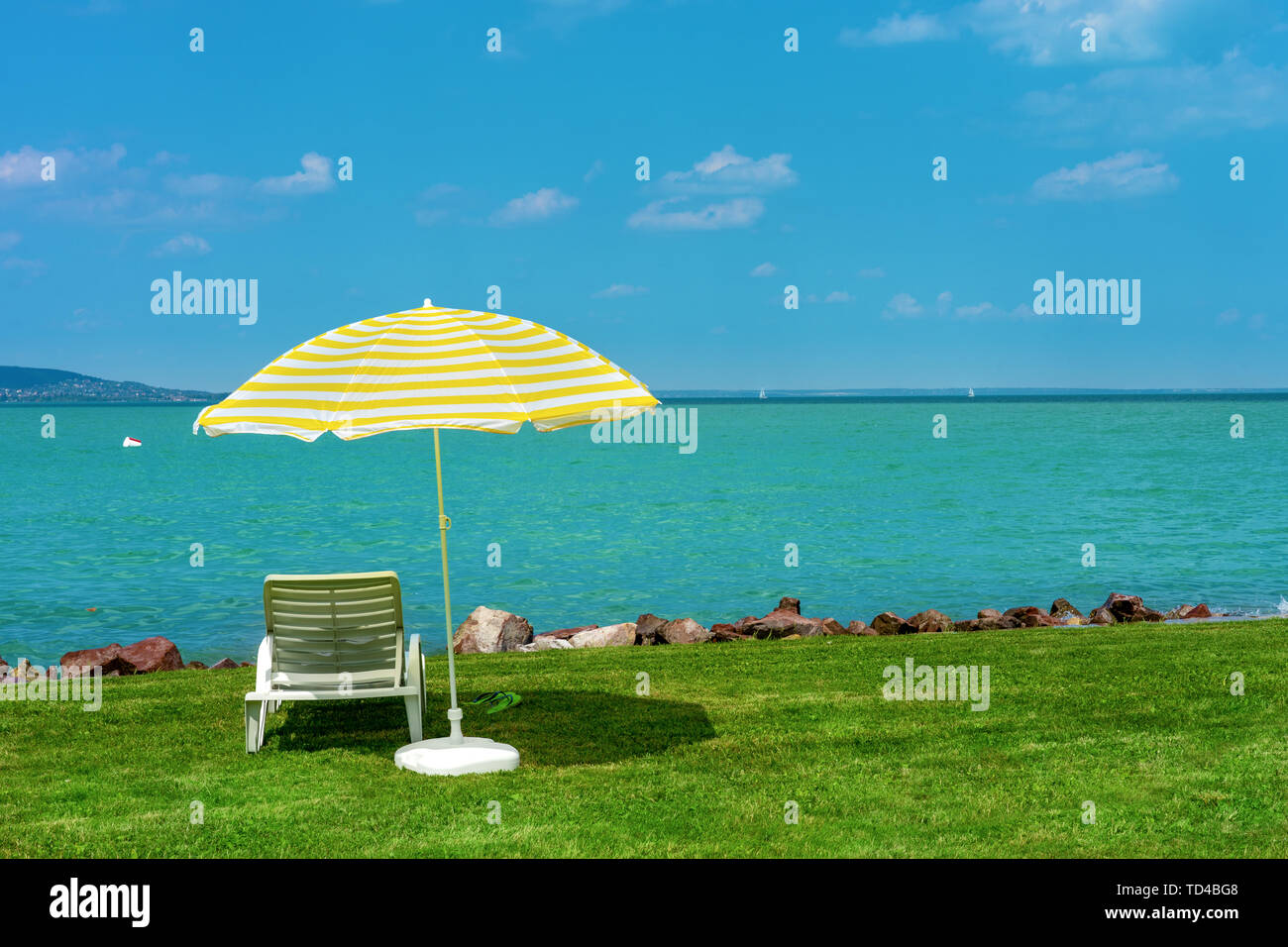 Chaise longue chaise longue en plastique élégant avec des rayures jaune parasol parapluie de plage sur l'herbe verte sur la plage à été sous ciel ouvert. Transats destinés à Banque D'Images