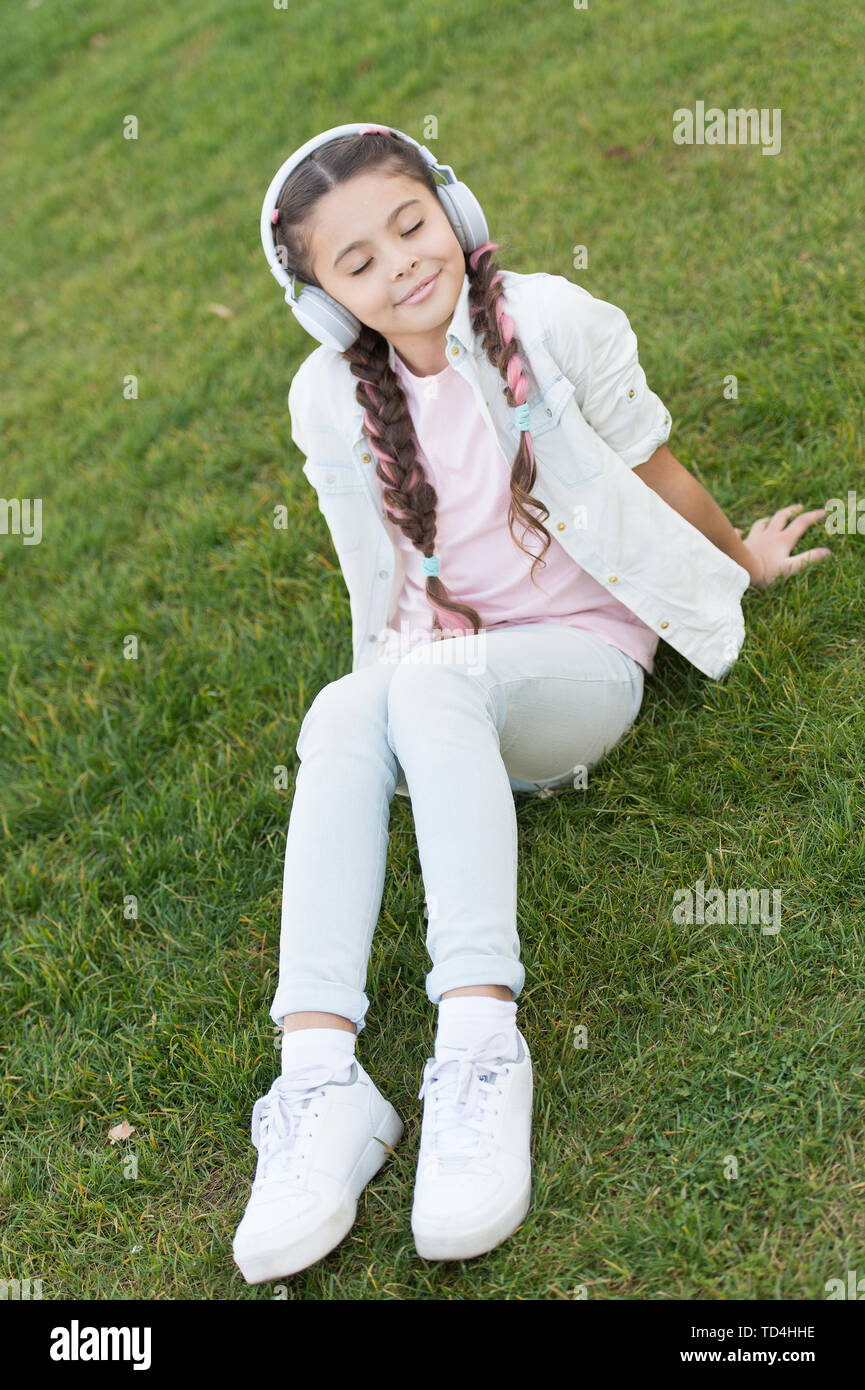 Écouter de la musique douce son est tout à fait relaxant de moi. Petite  fille de l'écoute la voie sur l'herbe verte. Petit enfant wearing earphones  jouant son électronique. Cute kid bénéficiant