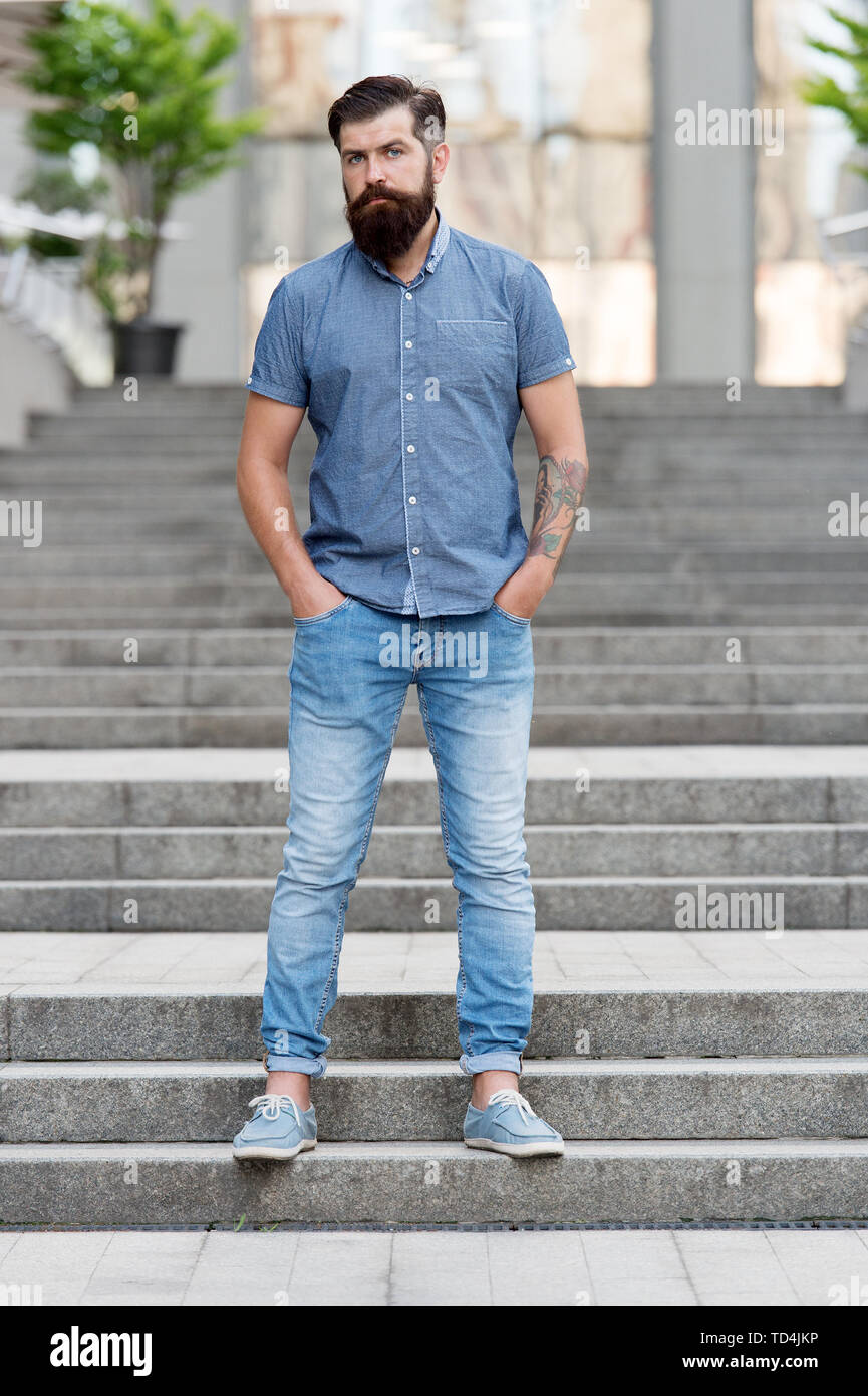 En amour avec le denim. Hipster barbu homme mannequin de porter des  vêtements en denim escaliers en fond urbain. Promenade régulière en  centre-ville. Confiant guy porter des jeans pantalon en jean et