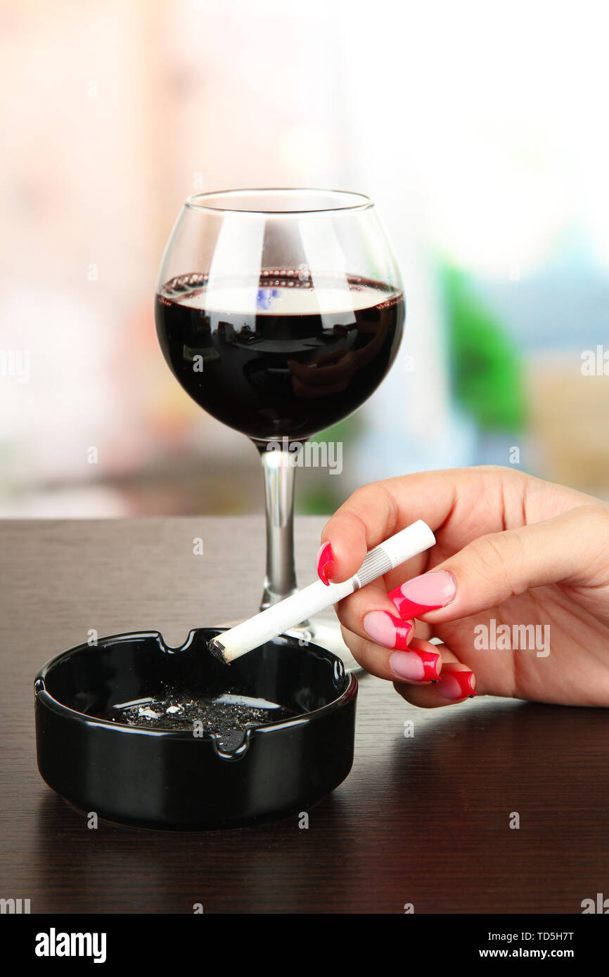 La main féminine avec verre à vin rouge et la cigarette, sur fond lumineux Banque D'Images