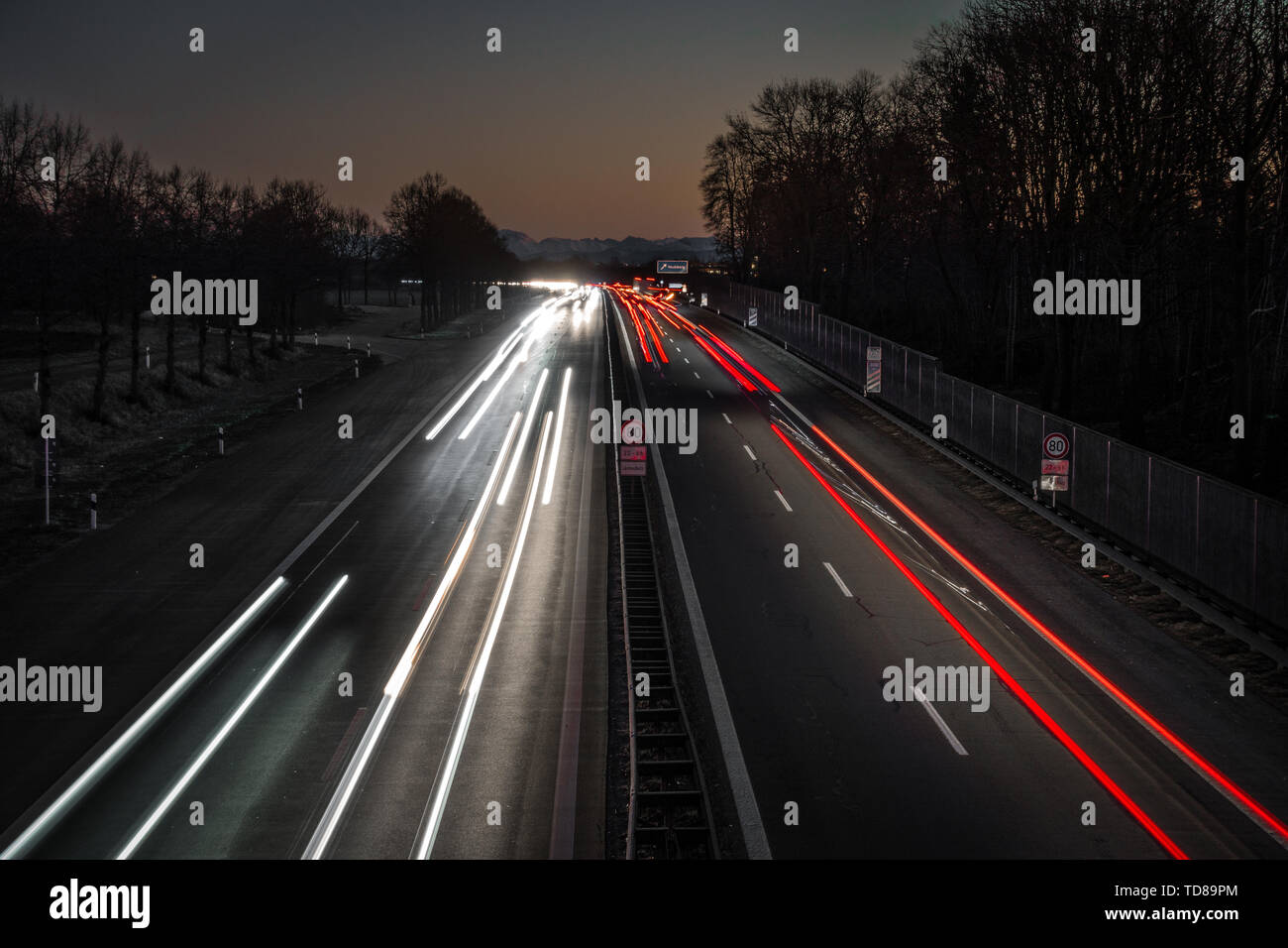 L'autoroute menant à des alpes par le coucher du soleil. Vous pouvez voir les sentiers de la lumière des voitures et la dernière de rougeoyant coucher du soleil dans les Alpes. Banque D'Images