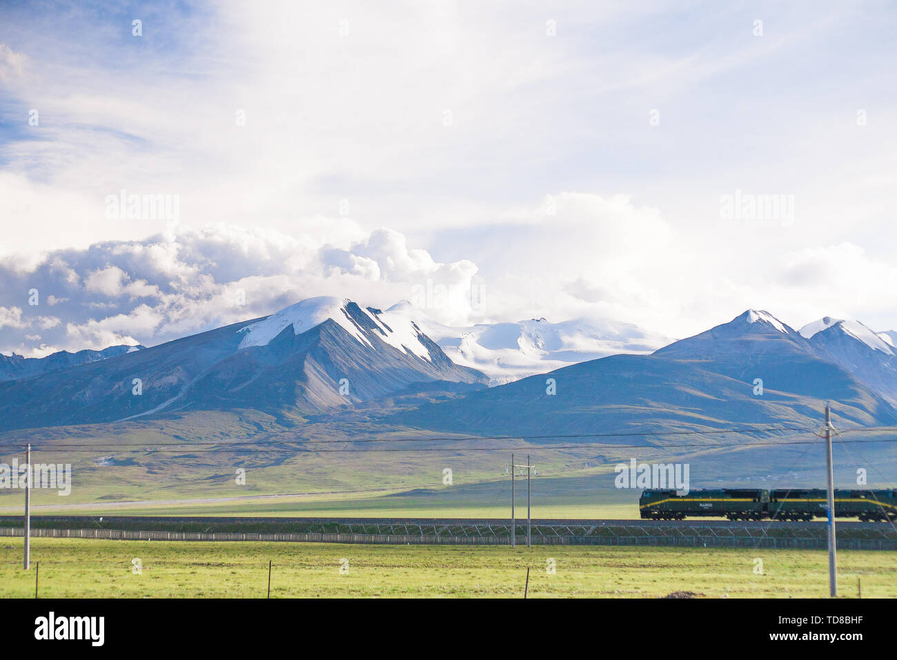 En été, un train de voyageurs sur la ligne Qinghai-Tibet fonctionne dans les montagnes enneigées. Banque D'Images