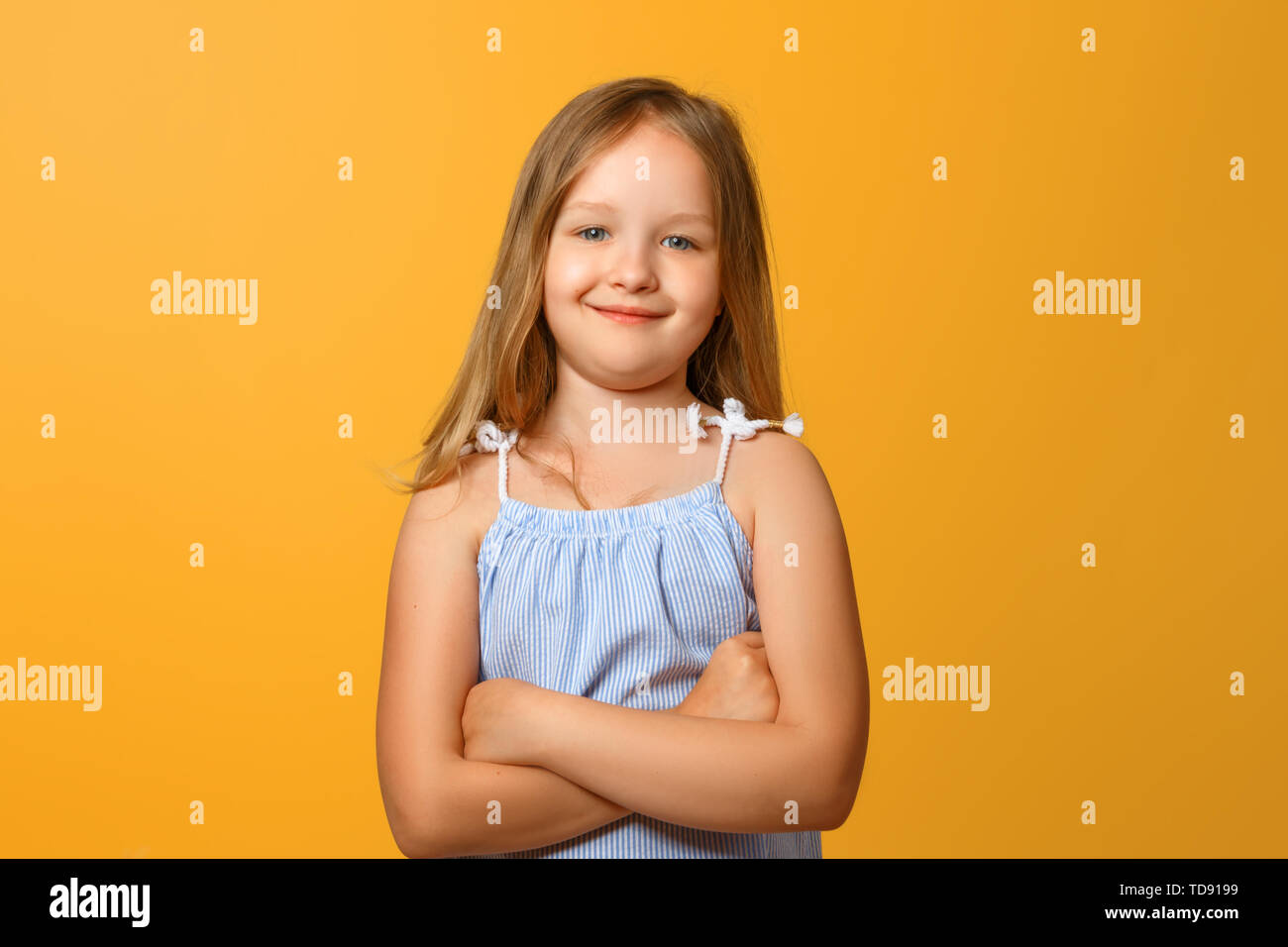 Closeup portrait d'un drôle de petit fille blonde sur un fond jaune. L'enfant croisa les bras et se penche sur l'appareil photo. Banque D'Images