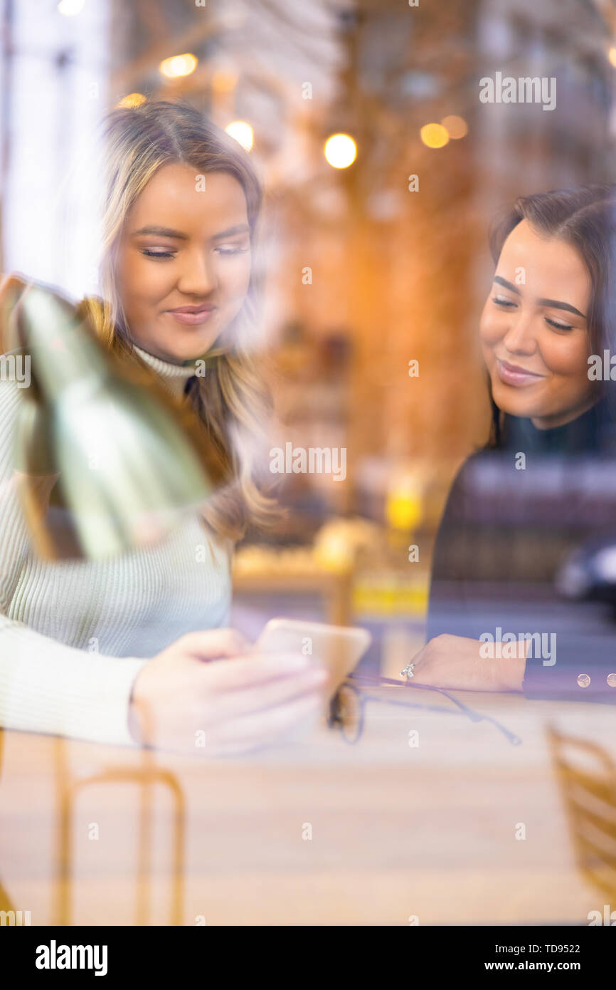 Deux amies Looking At Smartphone In Cafe vu à travers la vitre Banque D'Images