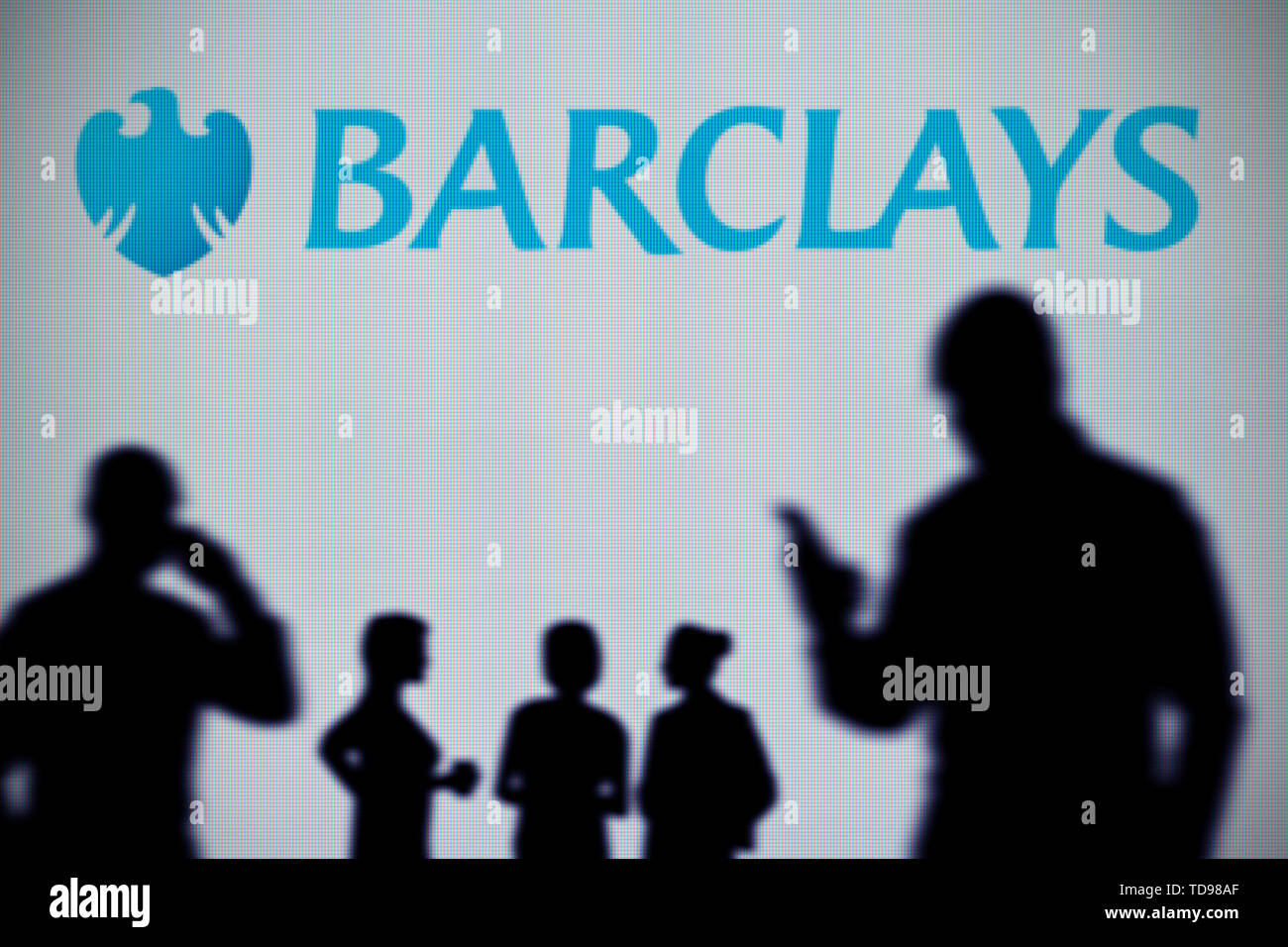 Le logo de la banque Barclays est vu sur un écran LED à l'arrière-plan tandis qu'une personne utilise la silhouette d'un smartphone dans l'avant-plan (usage éditorial uniquement) Banque D'Images