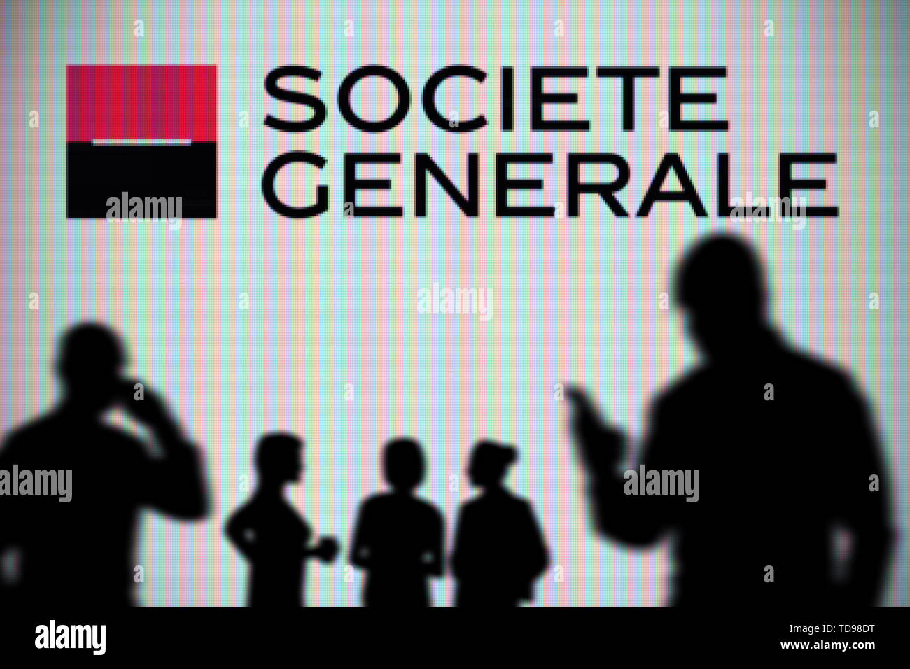 Le logo Société Générale est vu sur un écran LED à l'arrière-plan tandis qu'une silhouette personne utilise un smartphone (usage éditorial uniquement). Banque D'Images