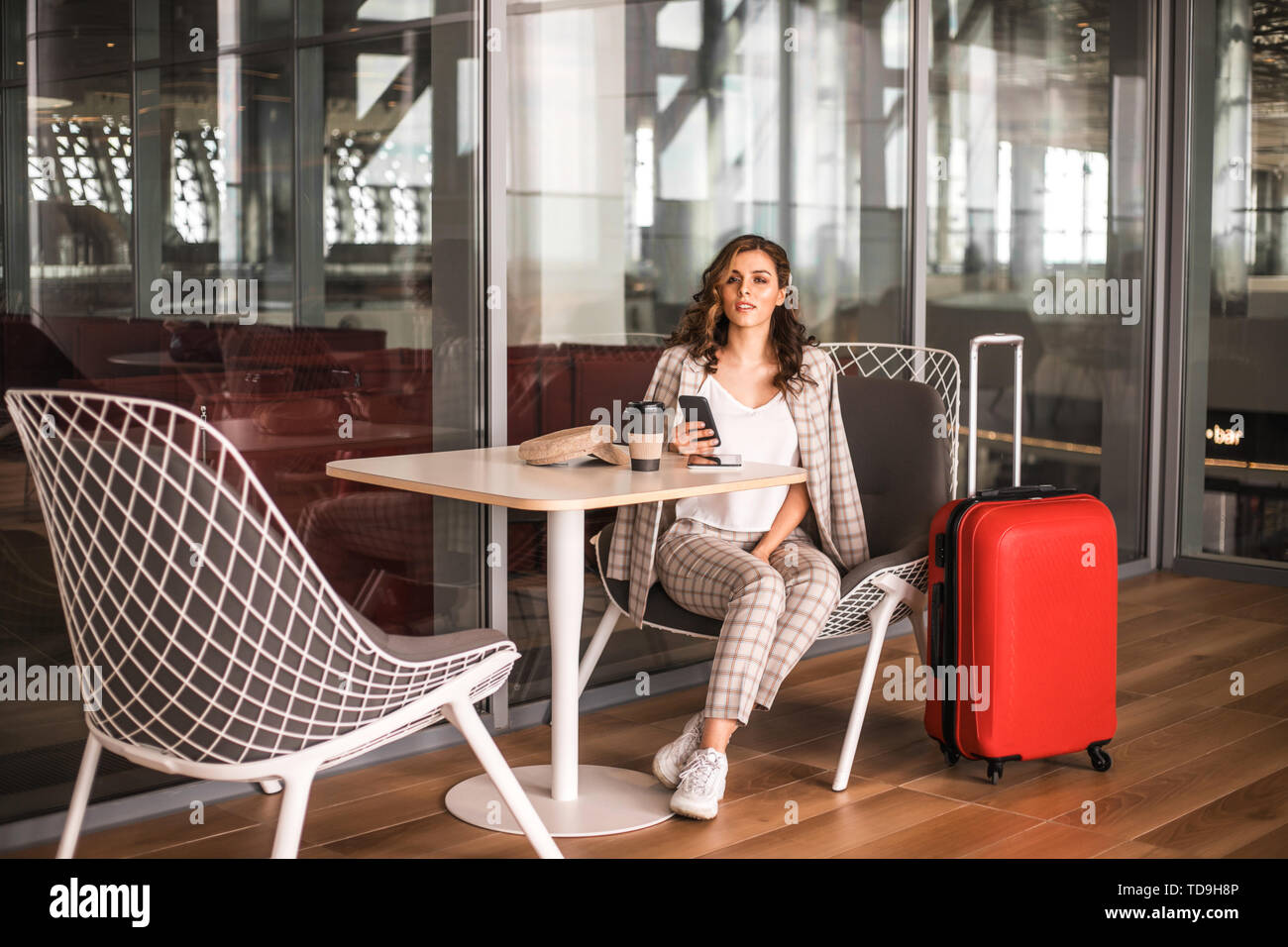 Belle femme d'affaires avec le smartphone en attente de son vol dans un aéroport. Banque D'Images