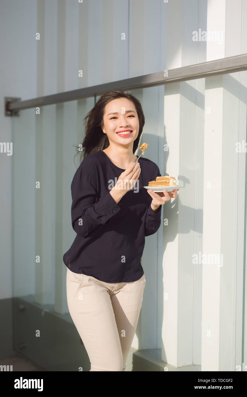 Jeune femme heureuse se tient sur la terrasse de l'hôtel avec des gâteaux dans la matinée. Jolie fille asiatique dans la bonne humeur et est prêt pour l'aventure. Banque D'Images