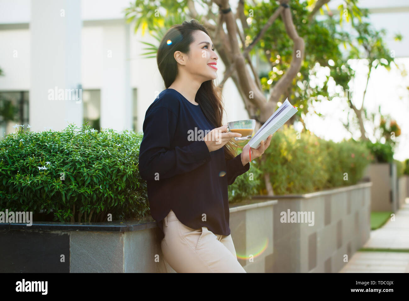 Happy young woman holding book friands de l'analyse de la littérature roman durant les loisirs sur terrasse de café campus en journée ensoleillée. Banque D'Images