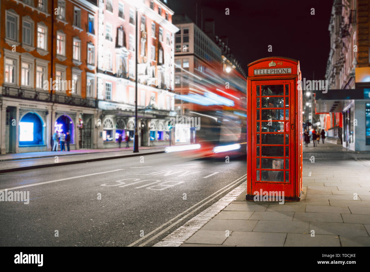 Les sentiers de la lumière d'un bus à deux étages à côté de l'emblématique cabine téléphonique à Londres Banque D'Images