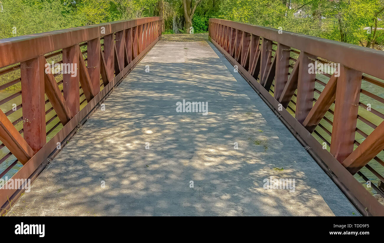 Pont cadre Panorama avec rusty garde-corps métalliques au-dessus d'un lac vue sur une journée ensoleillée. Le vert des feuilles des arbres ombres sur le pont d'e Banque D'Images