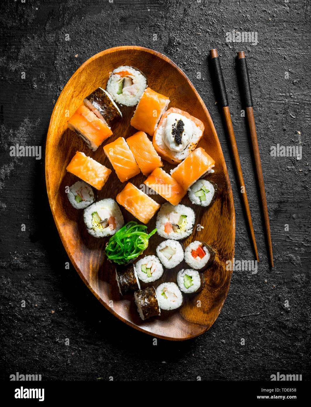 Différents rouleaux de sushi avec le saumon et les légumes sur une plaque de bois avec des baguettes. Noir sur fond rustique Banque D'Images