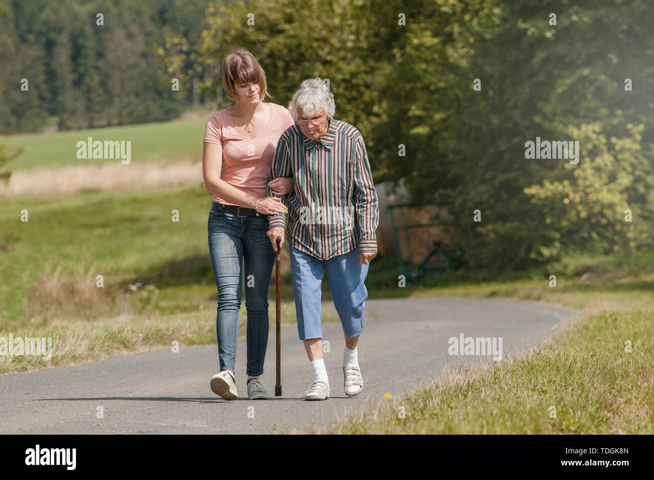 Jeune femme aide senior woman walking with stick Banque D'Images