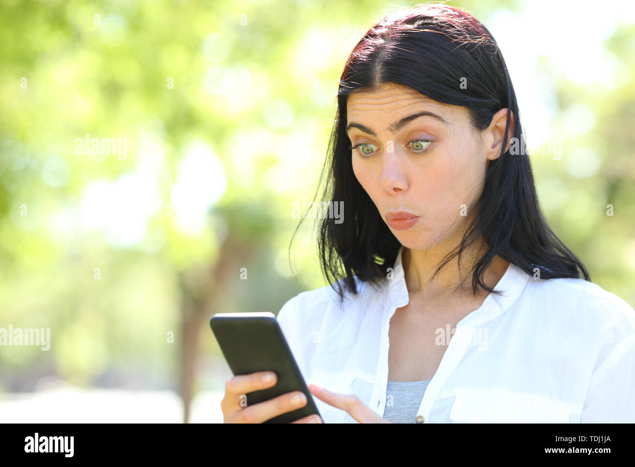 Perplexe woman reading smart phone contenu dans un parc avec un fond vert Banque D'Images