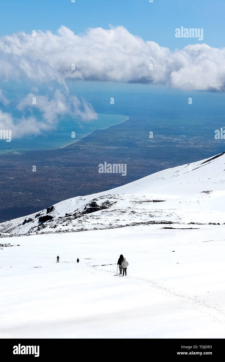 Superbe paysage pris du Mont Etna, en Sicile, Italie. Les randonneurs sur le chemin vers le bas du volcan. La neige sur la montagne. La côte de la mer de Sicile en arrière-plan. Destination de voyage populaires. Banque D'Images