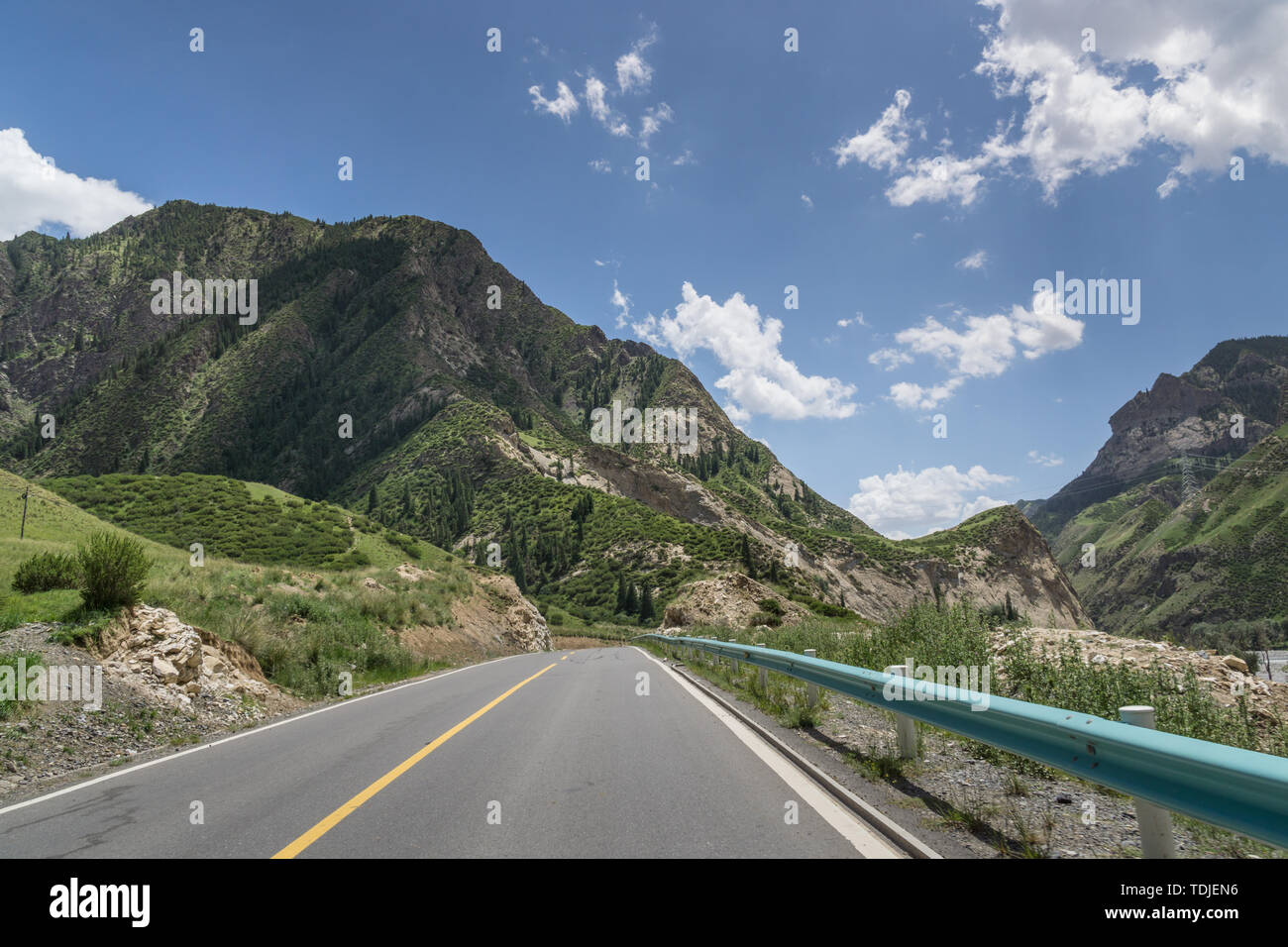 G217 Duku autoroute dans la forêt de l'Été alpin sous ciel bleu et nuages blancs dans le Xinjiang, Chine Banque D'Images