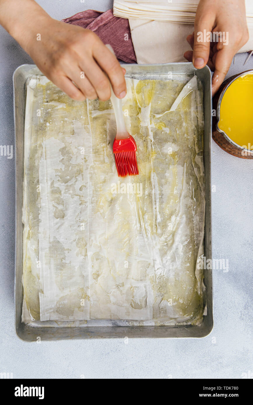 Femme répandre le beurre fondu sur les feuilles de pâte filo baklava avec un pinceau dans une plaque à pâtisserie Banque D'Images