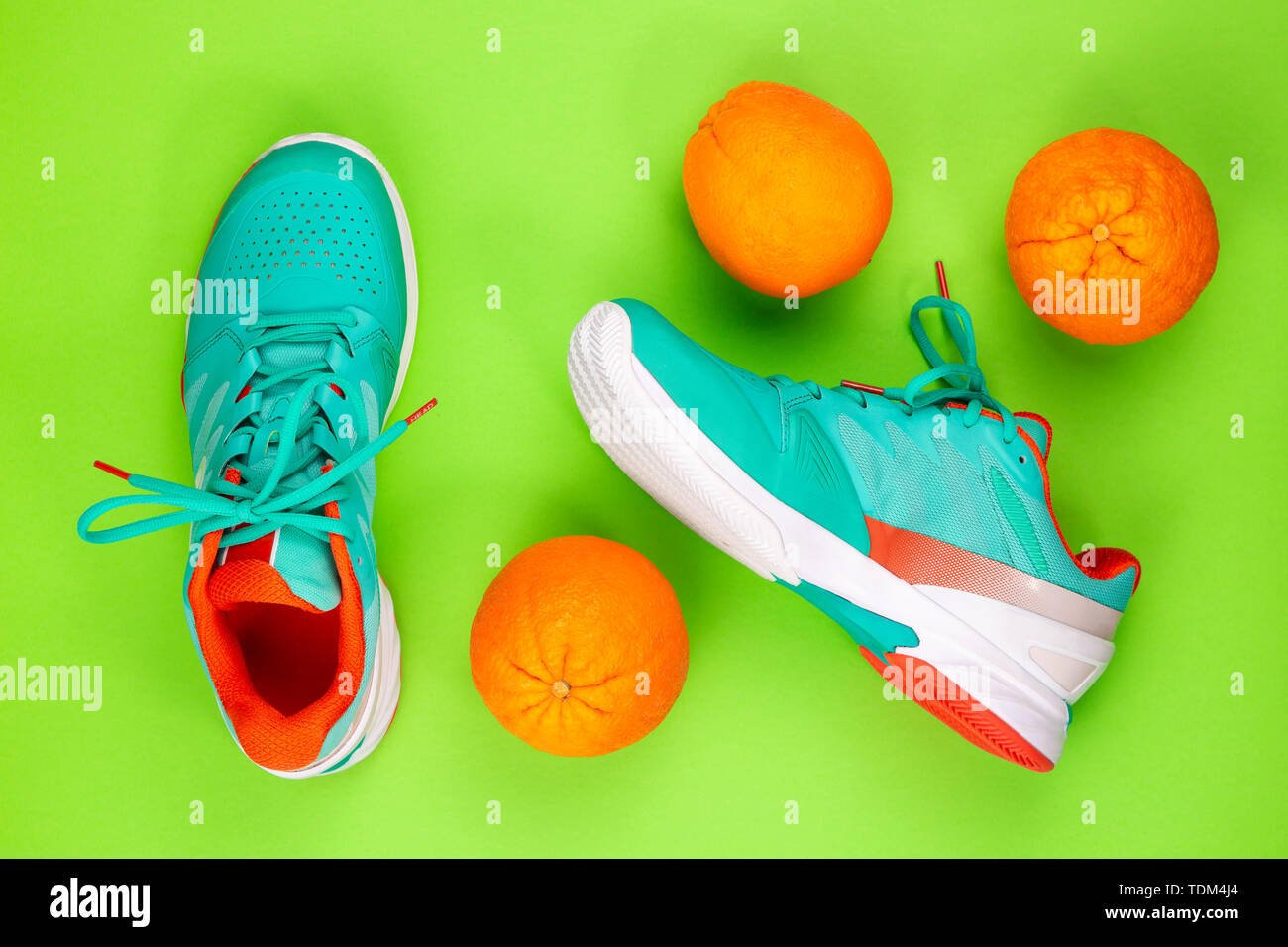 Cyan, rouge, blanc paire de chaussures de tennis en studio shot sur fond vert avec des oranges à côté d'eux. Directement à partir de ci-dessus. Banque D'Images