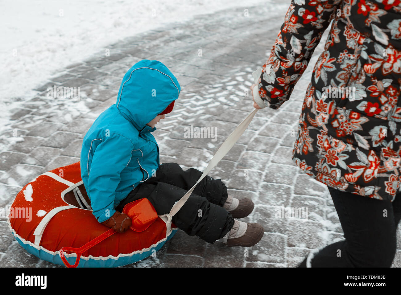 Petit garçon sur un traîneau en hiver. maman bébé tire le tube sur le bas de la rue Banque D'Images