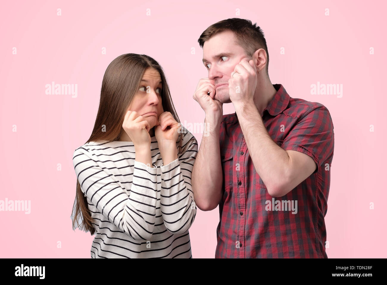 Drôle jeune couple qui s'étend sur la peau des joues étrange grimace Banque D'Images