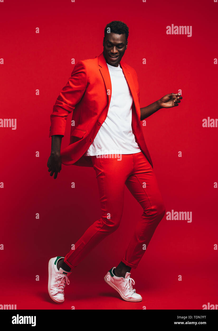 Toute la longueur od beau jeune homme africain dansant sur fond rouge. L'homme en habit rouge élégant montrant quelques mouvements de danse. Banque D'Images