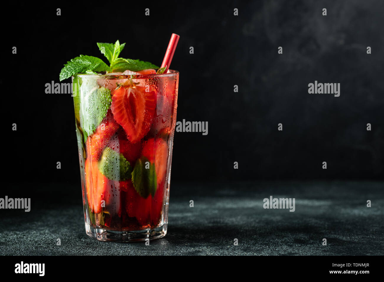 Limonade Fraîche avec de la glace, menthe et fraise sur le dessus en verre sur le tableau noir, l'arrière-plan de l'espace de copie. Boisson d'été froid. Verres étincelants avec berry co Banque D'Images