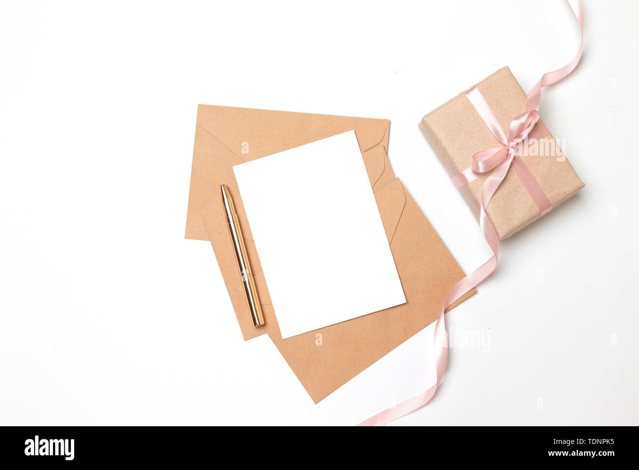 Enveloppe de papier kraft avec une feuille blanche et cadeau surprise fort avec ruban rose sur fond gris Banque D'Images