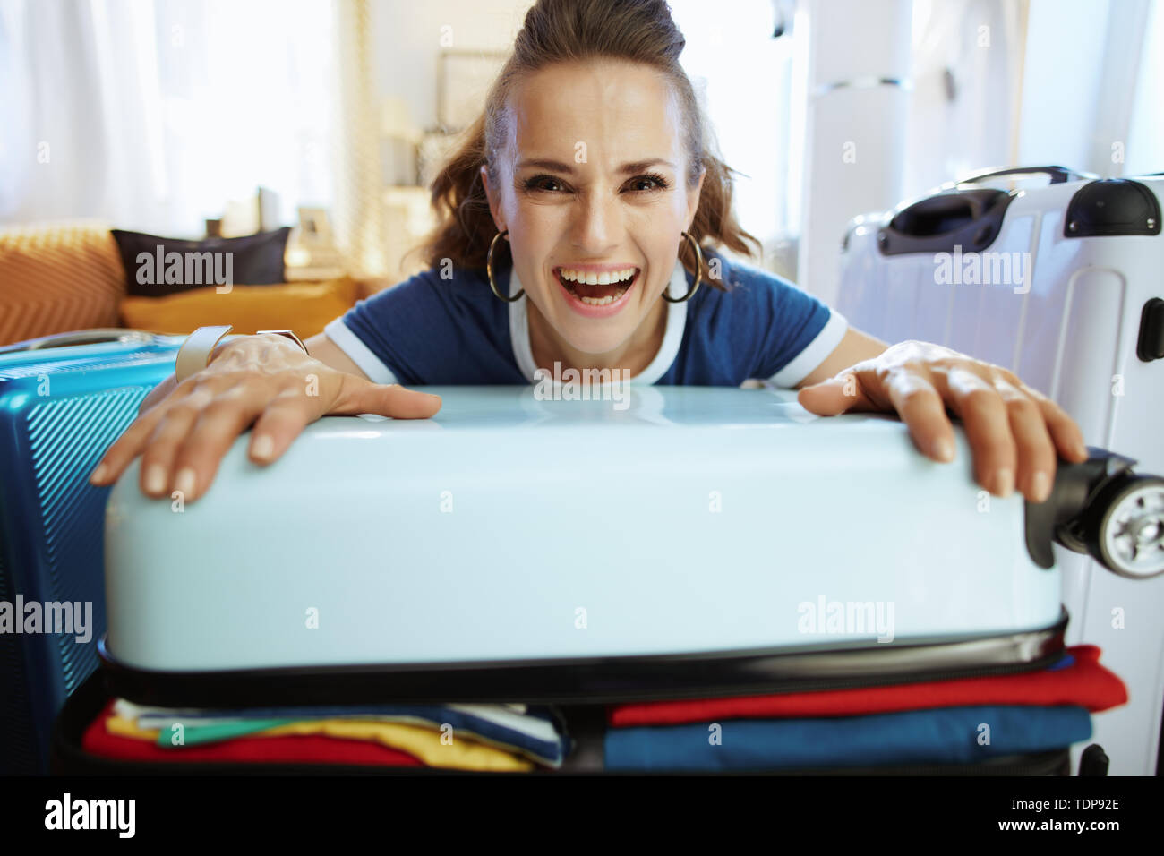 Portrait of happy femme moderne en bleu t-shirt dans la maison moderne en journée ensoleillée valise d'emballage. Banque D'Images