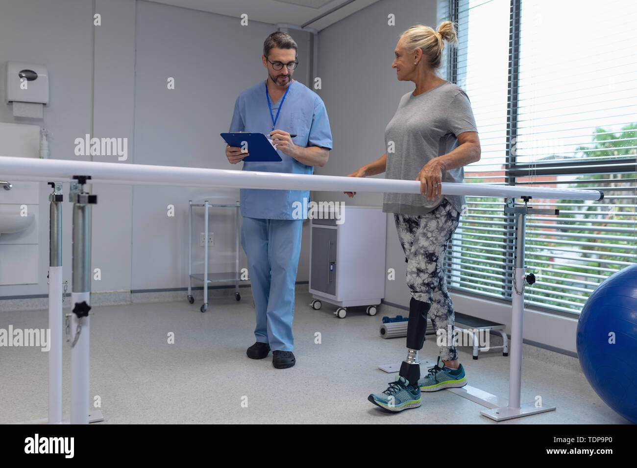 Physiothérapeute mâle writing on clipboard et le patient marche avec des barres parallèles Banque D'Images