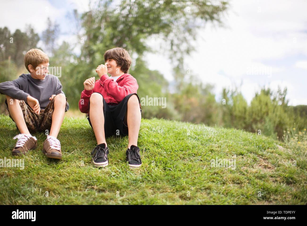 Deux smiling teenage garçons assis sur une banque d'herbe dans un parc. Banque D'Images