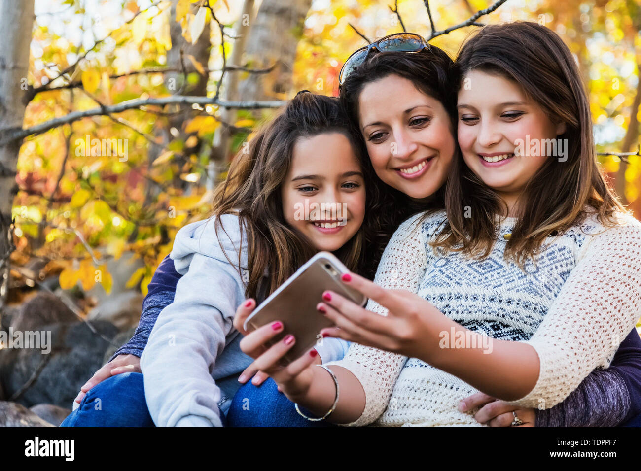 Une maman et ses deux filles en prenant un auto-portrait au repos pendant une sortie en famille dans un parc de la ville sur une chaude journée d'automne ; Edmonton, Alberta, Canada Banque D'Images