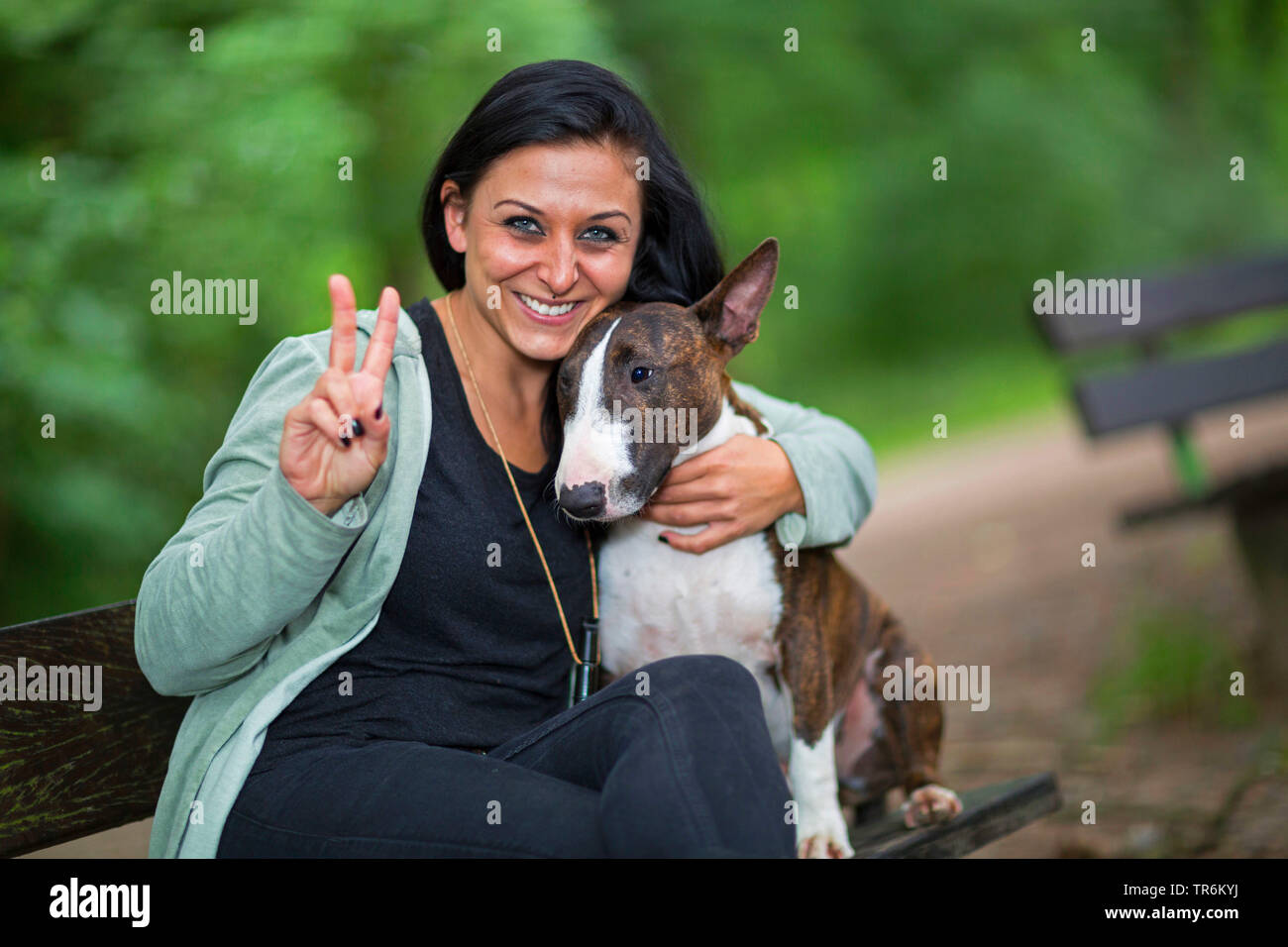 Bull Terrier (Canis lupus f. familiaris), homme chien smooching avec sa maîtresse dans une forêt sur un banc, Allemagne Banque D'Images