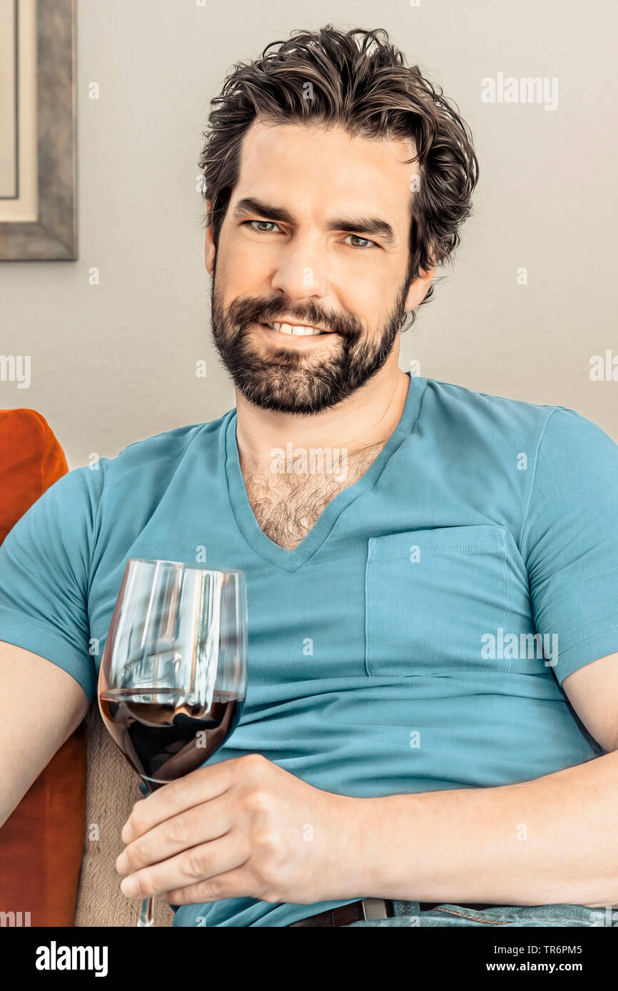 Mann mit Bart sur le canapé avec un verre de vin rouge, Allemagne Banque D'Images