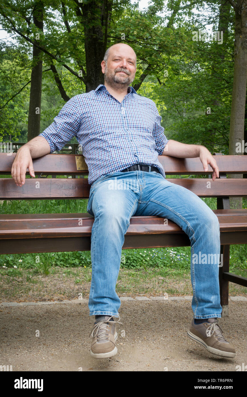 Homme avec barbe et tête chauve assis sur un banc dans la nature, Allemagne Banque D'Images