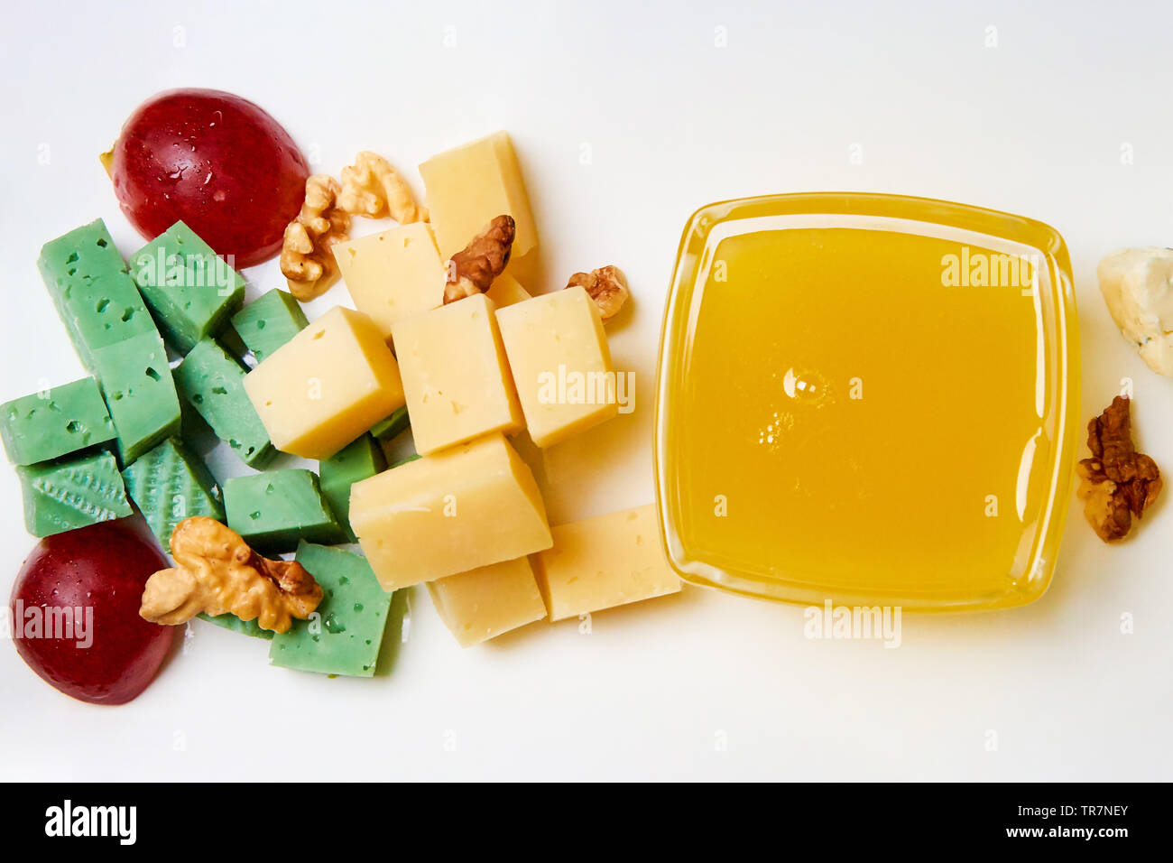 Fromage en tranches avec les noix, les raisins et le miel sur une plaque blanche. Banque D'Images