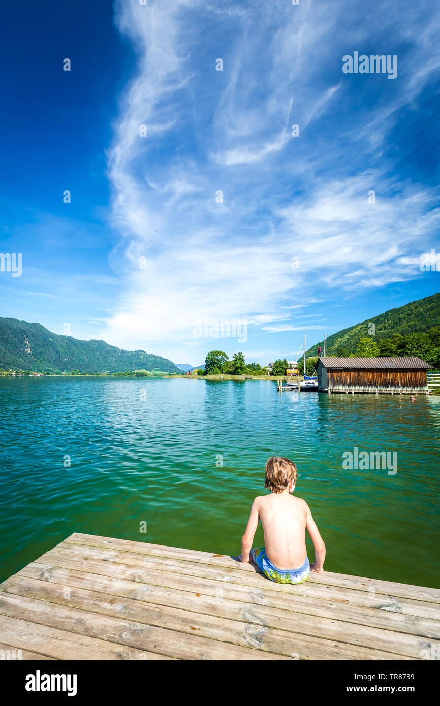 Garçon assis sur une jetée au lac Ossiacher See, Autriche Banque D'Images