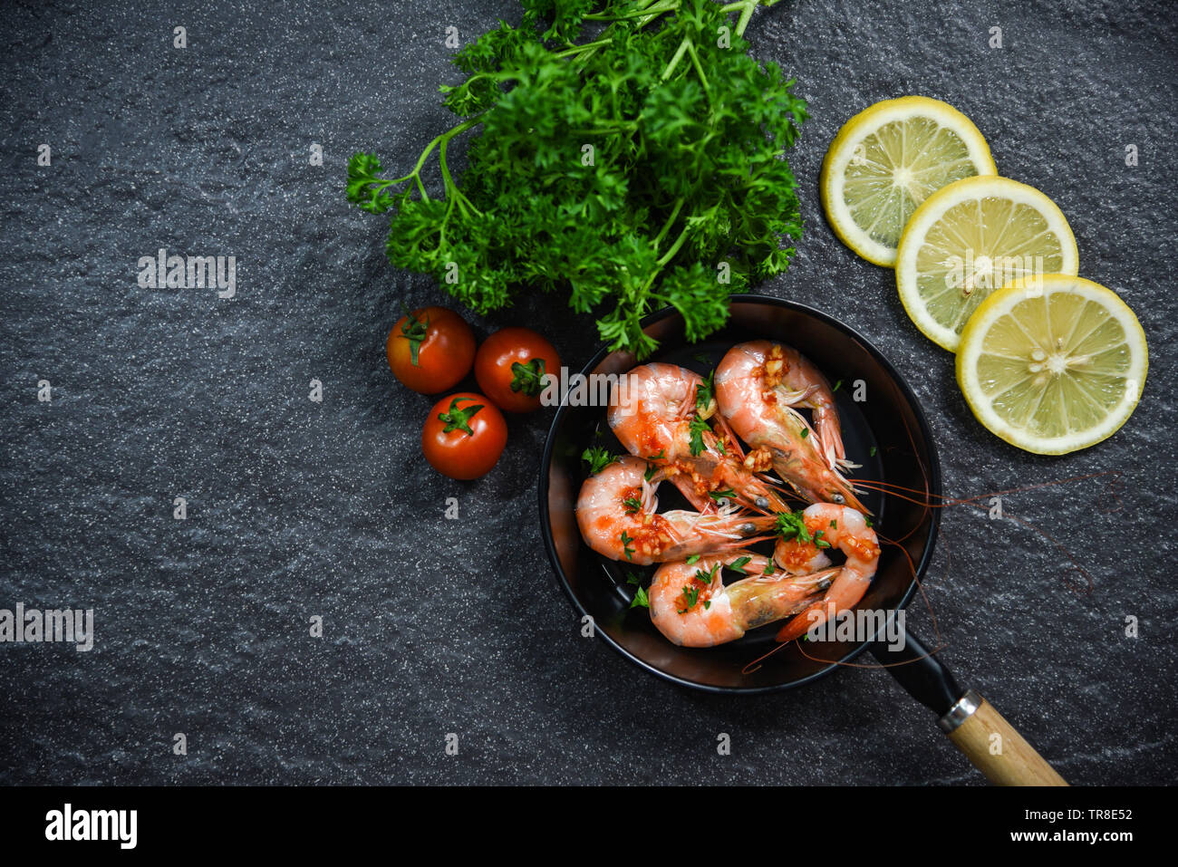 Fruits de mer aux crevettes Crevettes cuites à la poêle avec des herbes et épices tomate citron et persil frisé sur fond sombre Banque D'Images