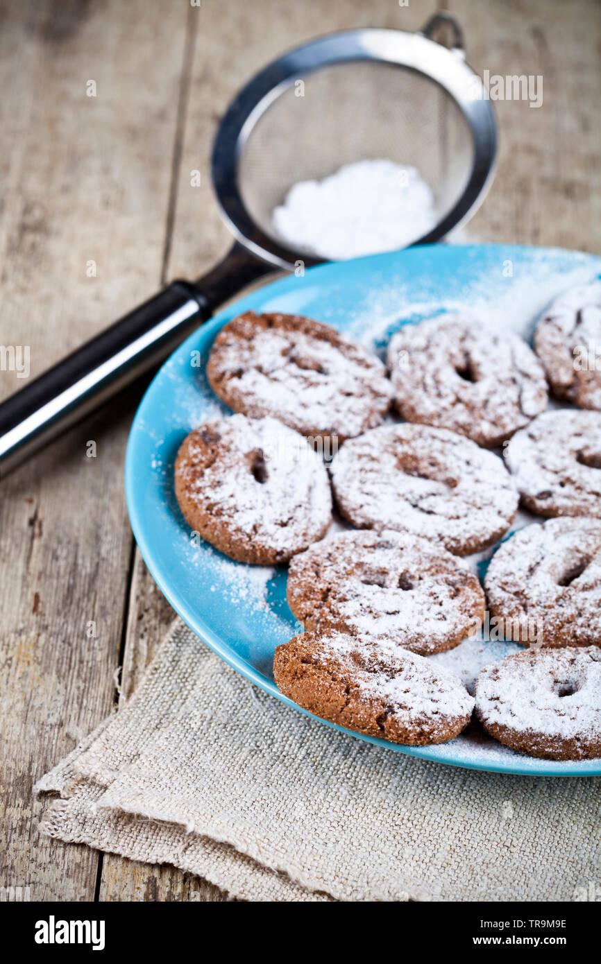 Fresh baked cookies au chocolat avec du sucre en poudre sur la plaque de métal bleu et crépine libre sur fond de table en bois rustique. Banque D'Images