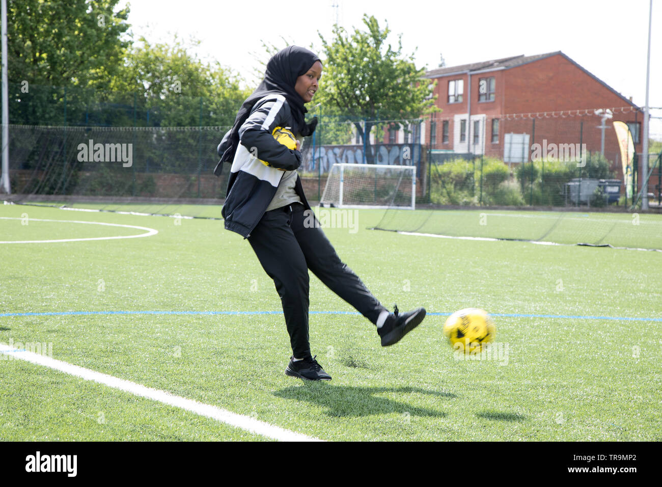 Une femme musulmane holding a football tire une balle de but sur un terrain de gazon synthétique Banque D'Images