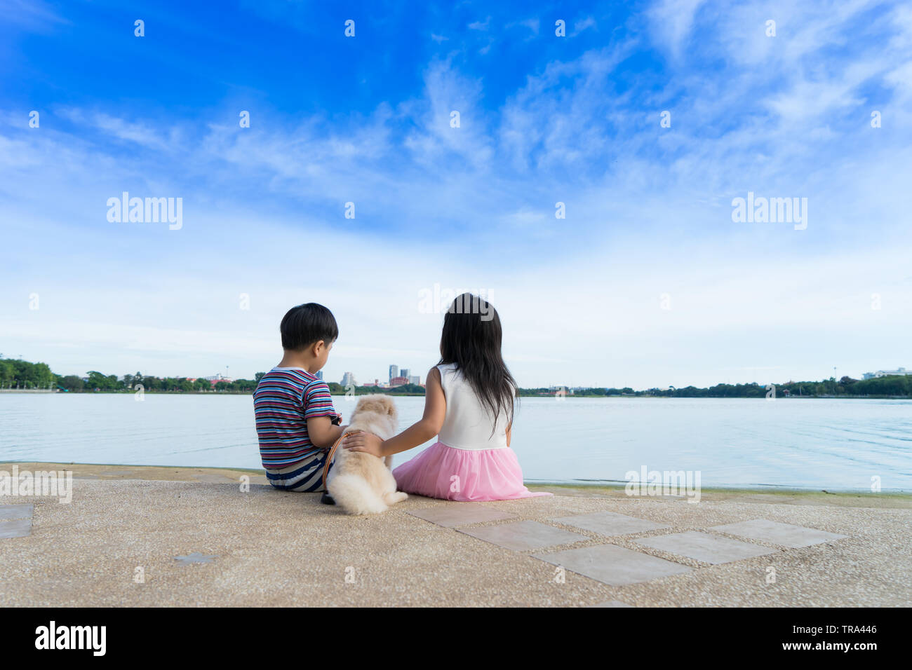 Petit Garçon et fille mignonne assis près de l'eau avec chien sur fond de ciel bleu, Banque D'Images