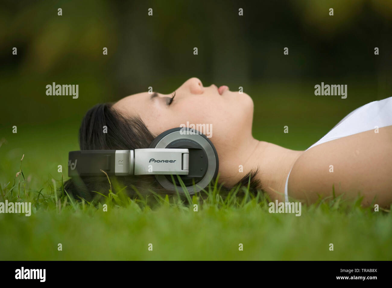 Amazing shot of a young Asian woman moderne reposant dans l'herbe fraîche portant des casques d'écoute de musique big Banque D'Images
