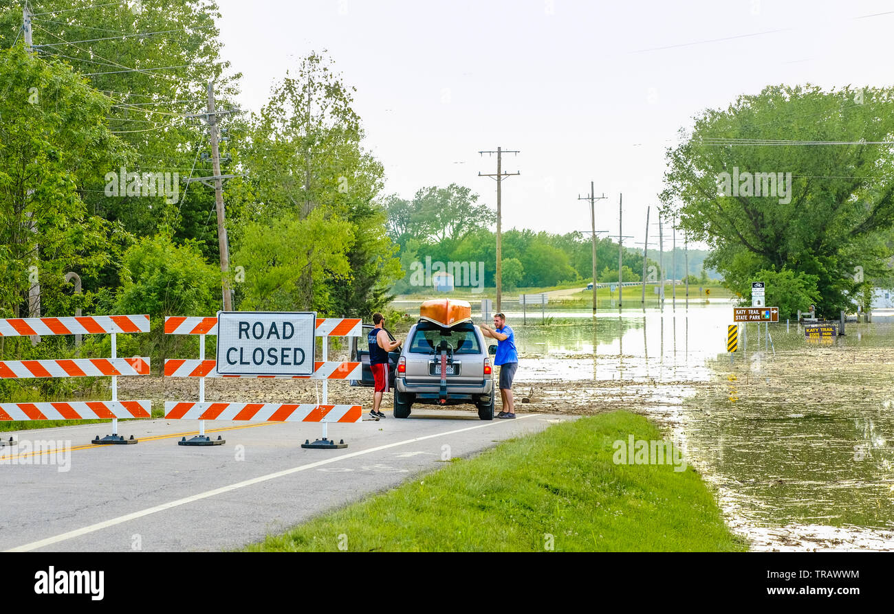 Vue de la route inondée près de McBain, Missouri, États-Unis ; deux jeunes hommes déchargeant leur canot à flotter le long de la route inondée Banque D'Images