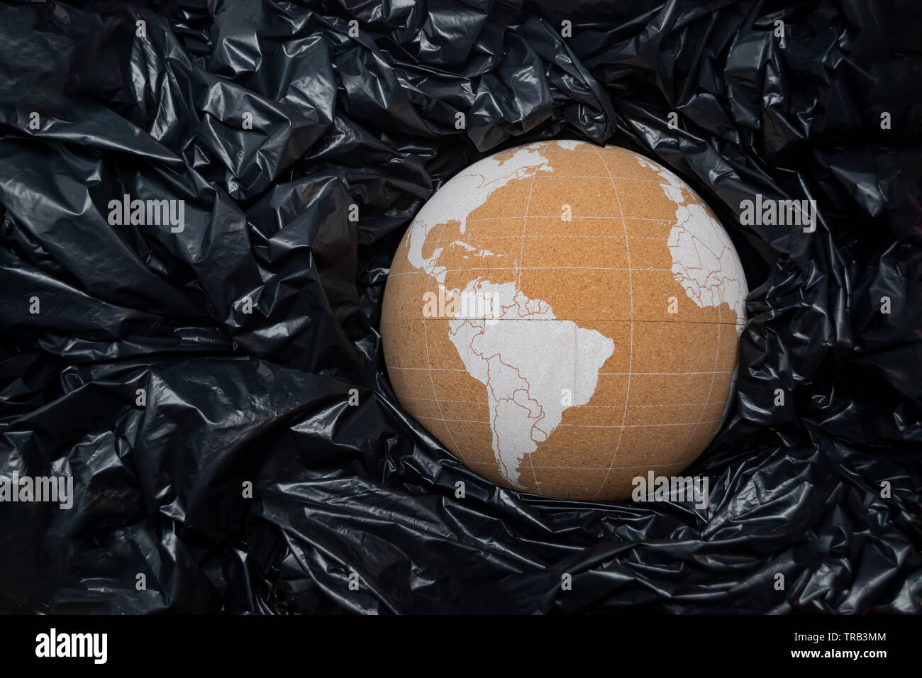 Cork globe représentant la planète Terre entre les sacs en plastique noir, d'amortissement. Problème de la pollution en plastique océan concept. Banque D'Images